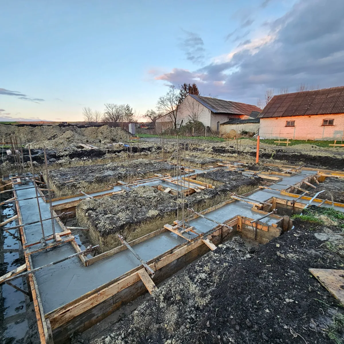 Fundamenty tradycyjne w wykopach z deskowaniem, zbrojeniem i świeżo wylaną betonową ławą