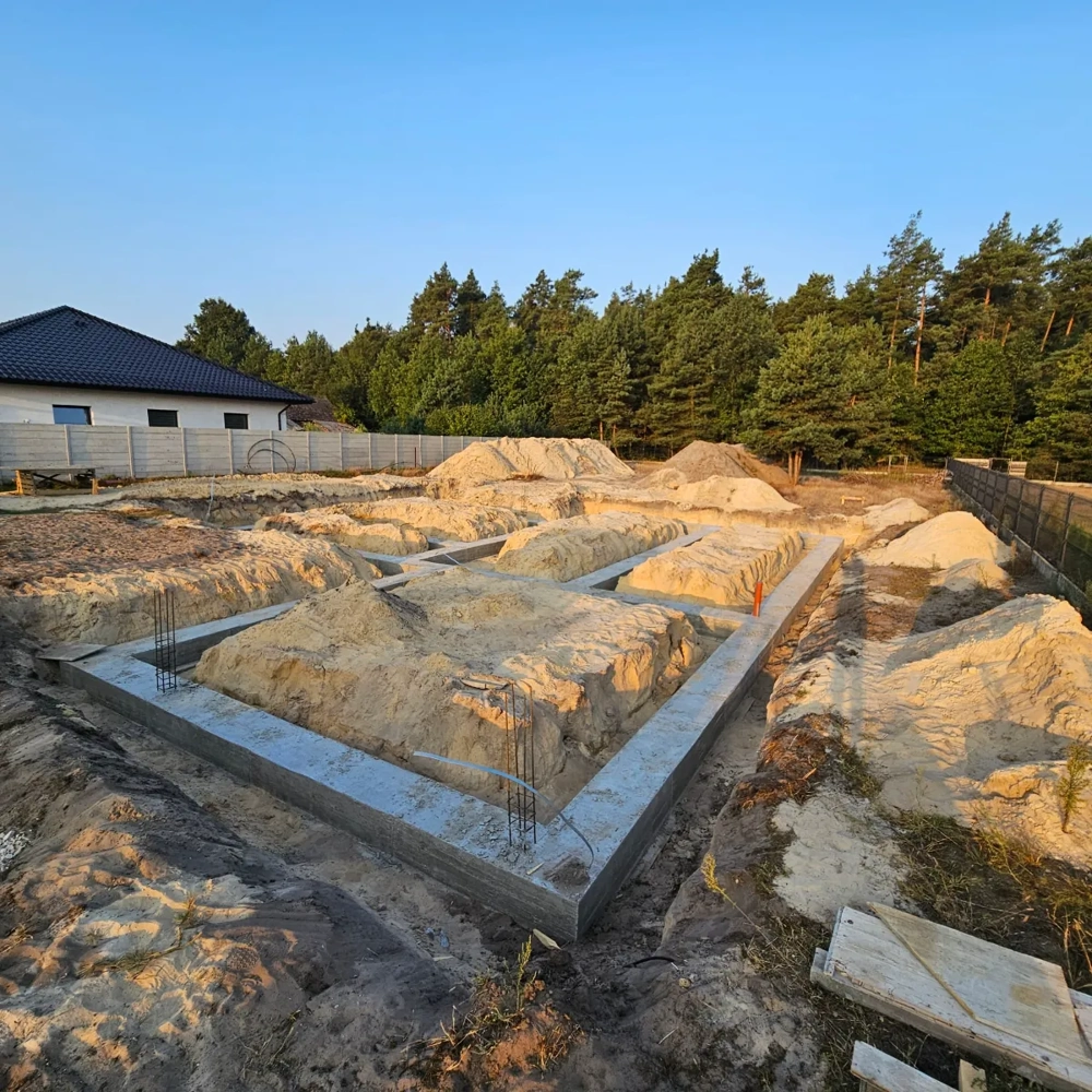 Betonowe ławy fundamentowe i zasypane wykopy pod fundamenty tradycyjne na terenie budowy domu z piaskiem i zbrojeniem