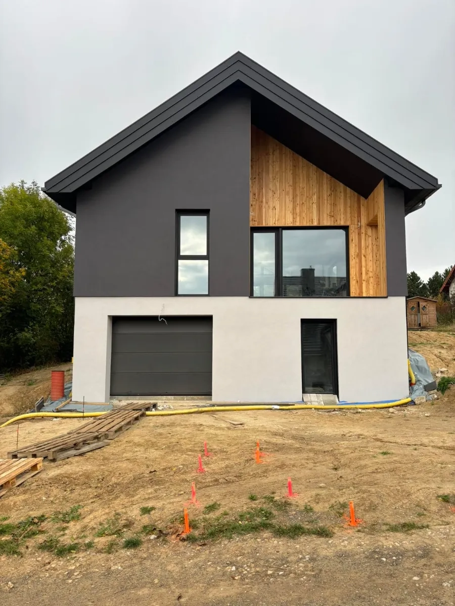 Dwupiętrowy nowoczesny dom z garażem i drewnianym wykończeniem elewacji na terenie budowy deweloperskiej Budowa domów