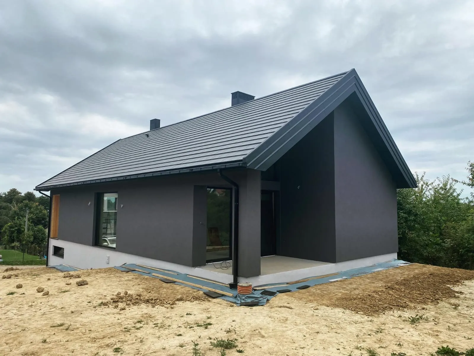 Elewacje domu nowoczesnej konstrukcji z ciemnym tynkiem, białą częścią fundamentową i metalowym dachem