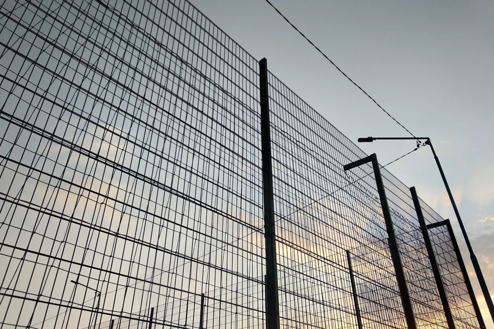 Ogrodzenia panelowe z metalowej siatki w świetle zachodzącego słońca i lamp ulicznych