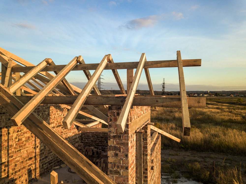 Więźba dachowa z drewnianych krokwi montowana na ceglanym murze budynku