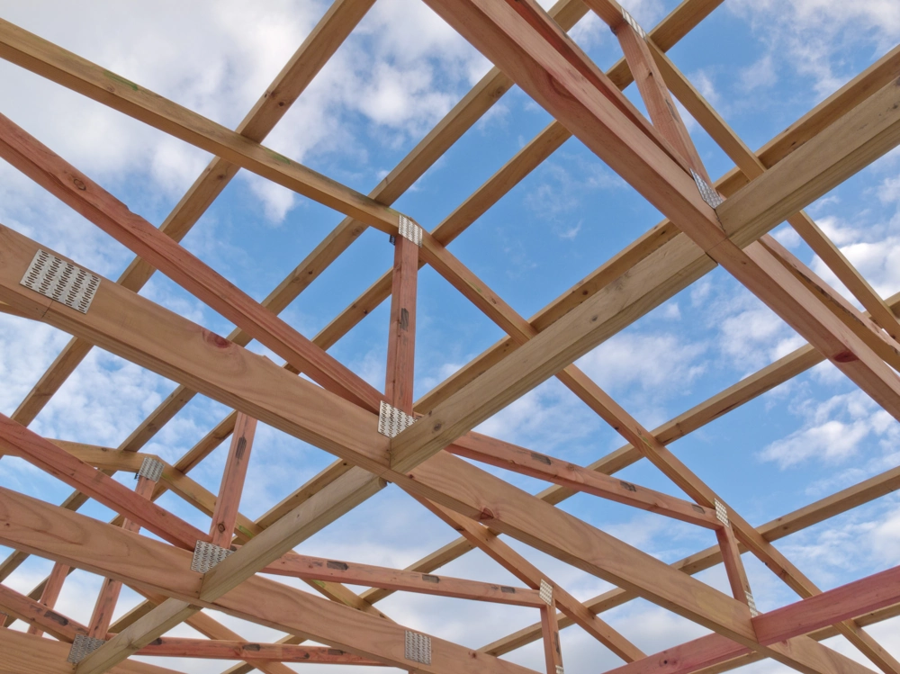 Drewniana więźba dachowa w trakcie montażu na tle błękitnego nieba